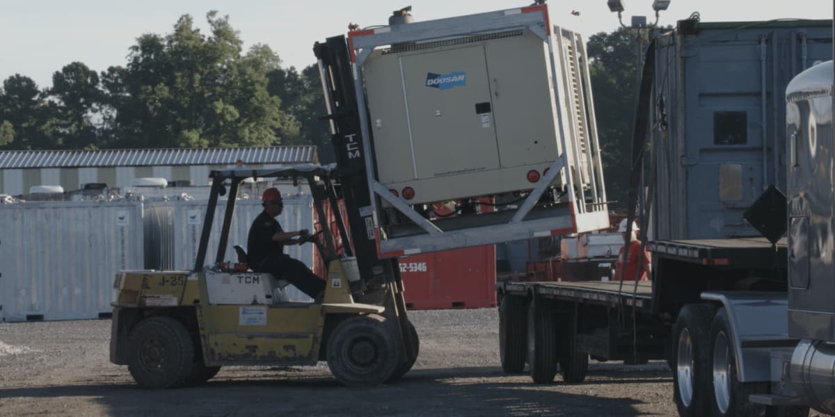 Forklift operator loading industrial equipment onto a transport truck
